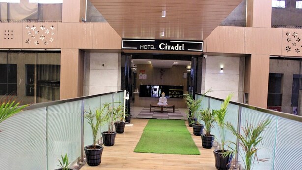 Un vestíbulo de hotel con un área de estar central, plantas en macetas y un cartel que dice 'HOTEL CITADEL'.