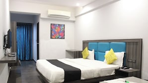 Habitación de hotel con cama, mesita de noche, escritorio con silla, aire acondicionado, un cuadro en la pared y una cortina azul.