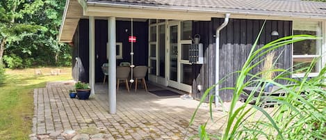 A covered outdoor area with a table and chairs, a potted plant, and a wooden fence.