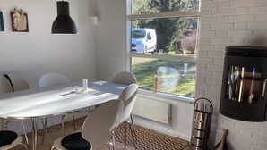 Une cuisine moderne avec une table blanche, des chaises, un poêle noir et une fenêtre donnant sur un fourgon blanc à l’extérieur.