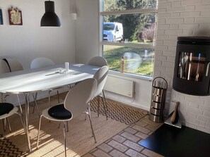 A modern kitchen with a white table, chairs, a black stove, and a window with a view of a white van outside. - 6 Person Holiday Home in Hals (Hals)
