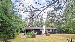 Une maison dotée d’un porche abrité, entourée d’une cour verdoyante et d’arbres.