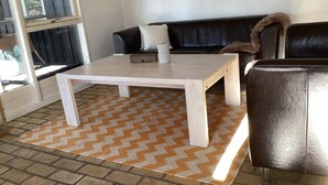 Un salon avec une table basse blanche, un canapé noir, un fauteuil en cuir marron et un tapis à motifs.