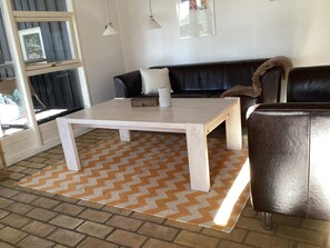 A living room with a white coffee table, a black sofa, a brown leather chair, and a patterned rug. - 6 Person Holiday Home in Hals (Hals)