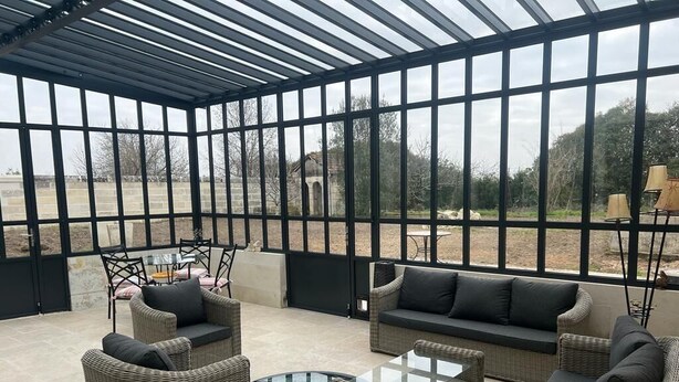 A covered outdoor seating area with wicker furniture and a glass coffee table.