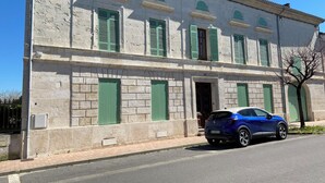 A building with a stone facade, green shutters, and a parked blue car.