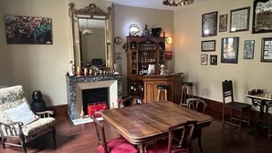 A dining area with a wooden table and chairs, a fireplace, a bar area with stools, and a collection of framed pictures on the wall.