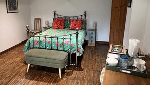 A bedroom with a bed, a bench, a bedside table, a nightstand, and a tray with cups and a picture frame.