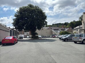 A parking lot with several cars, a large tree, and buildings in the background.