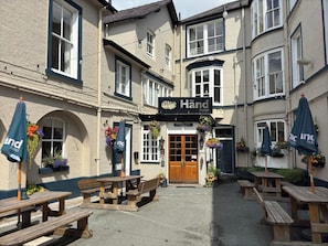 A traditional building with a sign reading 'The Hand Hotel,' outdoor wooden benches, and hanging flower baskets.