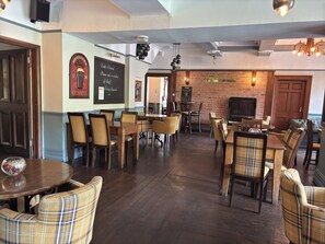 A restaurant interior with wooden tables and chairs, a brick wall, and a sign indicating a daily special.