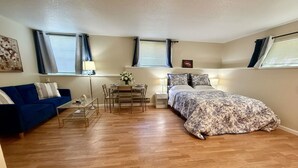 Een slaapkamer met een bed, een blauwe bank, een kleine tafel met een lamp, en een raam met gordijnen.