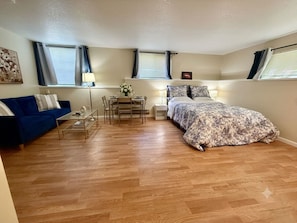 Un dormitorio con una cama, un sofá azul, una mesita con lámpara y una ventana con cortinas.