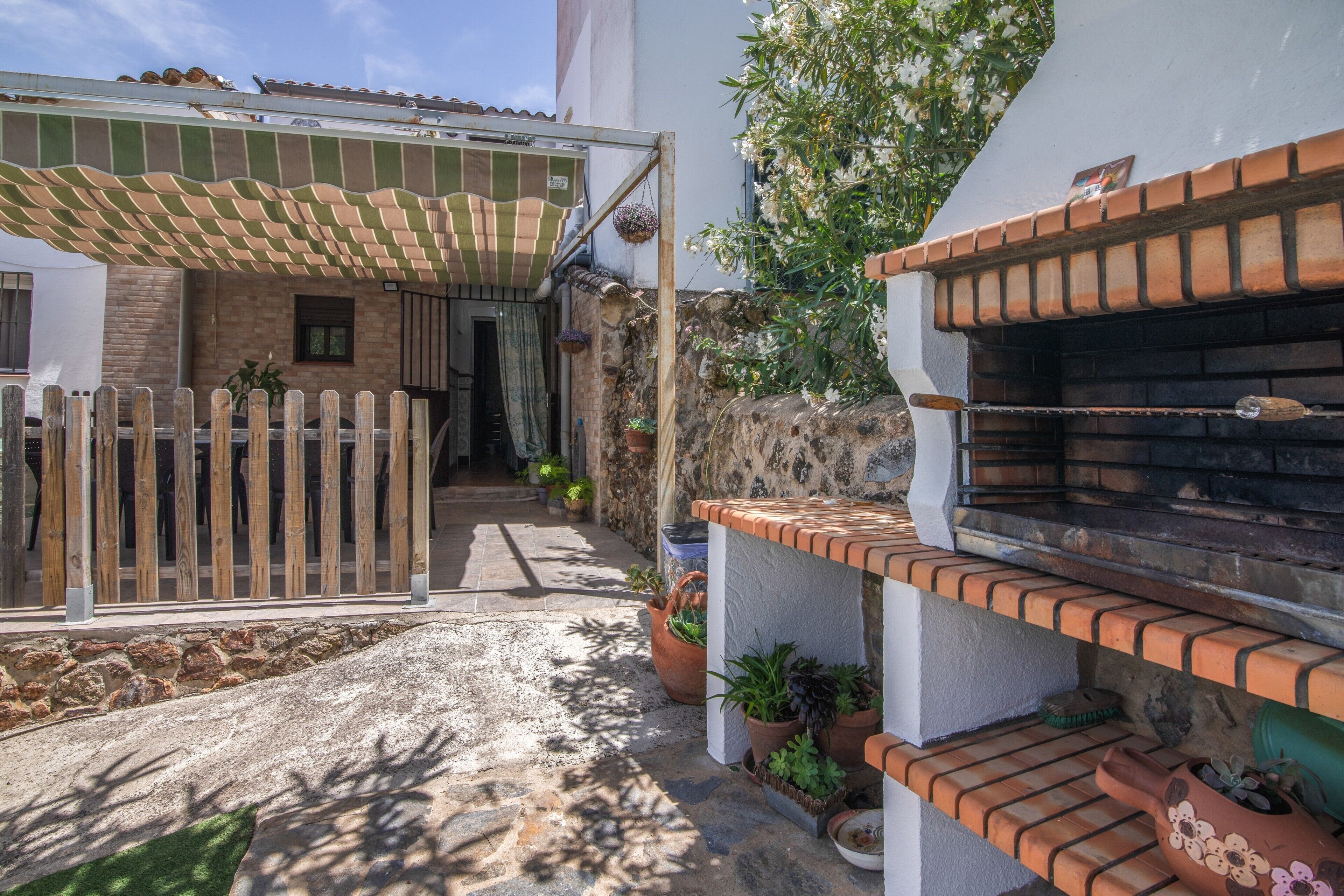 Un patio con un portón de madera, plantas en macetas, un horno de ladrillo y una zona de patio techada.
