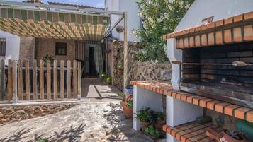Un patio con un portón de madera, plantas en macetas, un horno de ladrillo y una zona de patio techada.