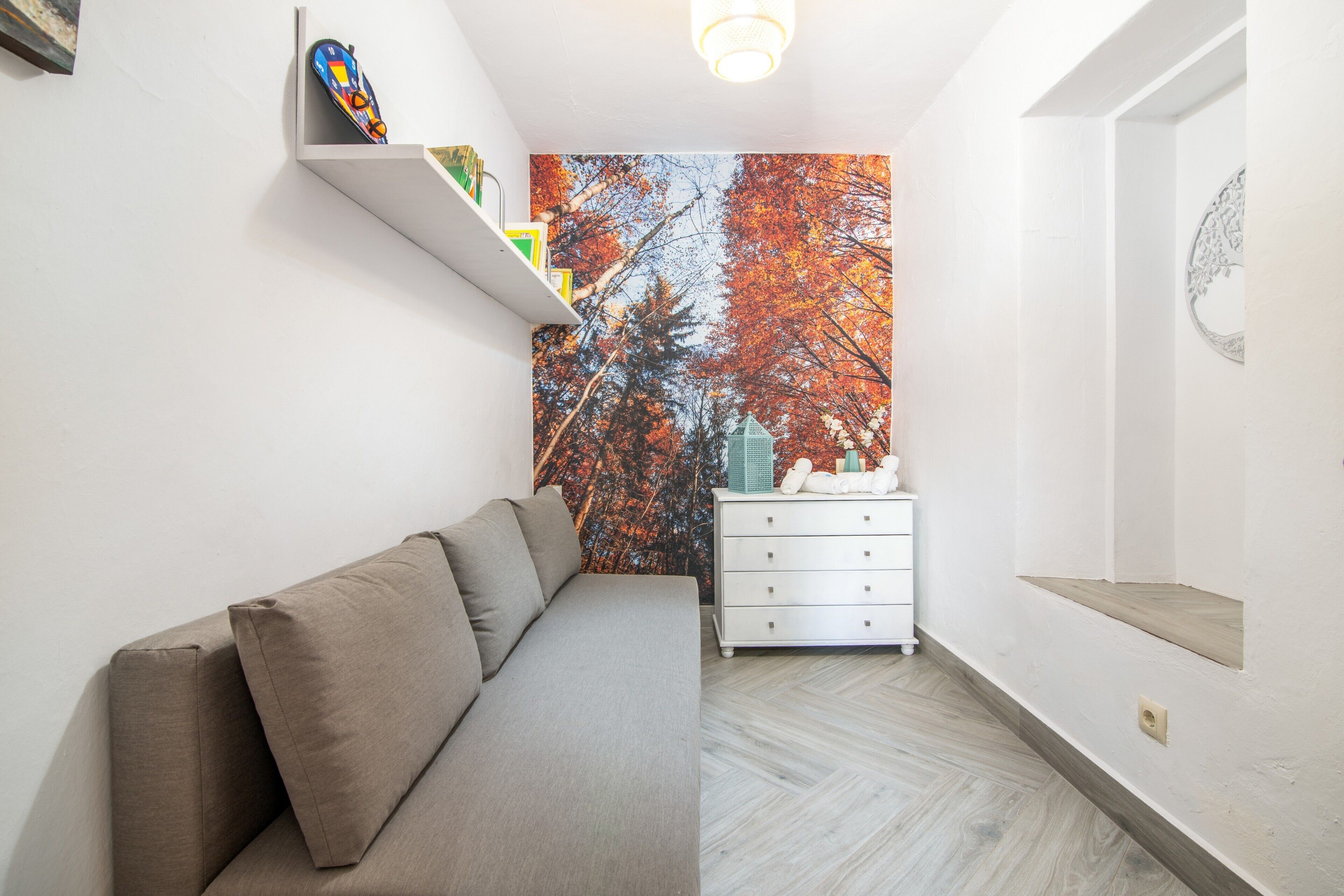 Una sala moderna con un sofá, un aparador blanco y un mural de árboles otoñales.