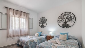 A bedroom with two beds, a nightstand, a window with sheer curtains, and two wall art pieces.