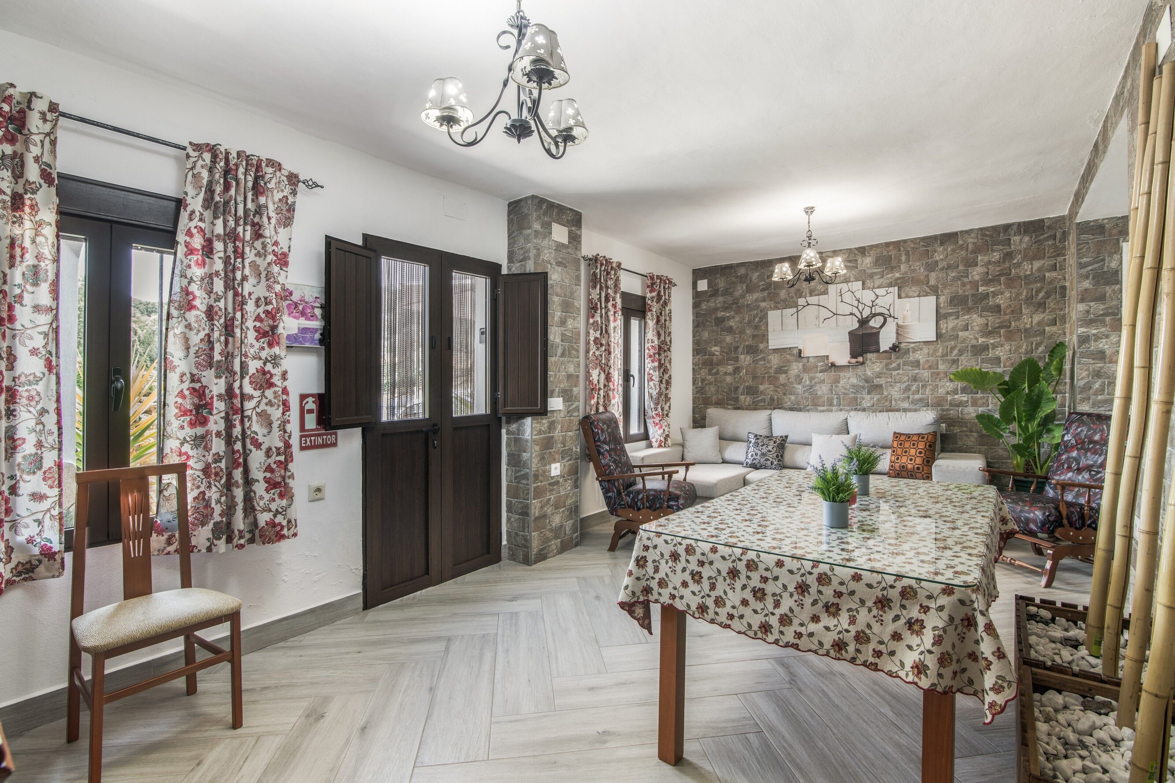 Una habitación con una mesa de comedor, sillas, un sofá, una planta en maceta y una pared de piedra.