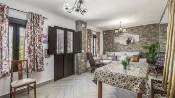 Una habitación con una mesa de comedor, sillas, un sofá, una planta en maceta y una pared de piedra.