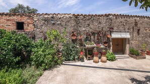 A rustic building with a stone wall, a wooden door, and various potted plants.