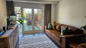 A living room with a brown leather sofa, a wooden desk with a computer, and a sliding glass door leading to a patio. - Scandi Garden Apartment (Stellenbosch)
