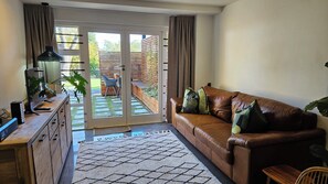 Ein Wohnzimmer mit einem braunen Ledersofa, einem Holztisch mit einem Computer und einer Glastür, die auf eine Terrasse führt.