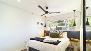A modern hotel room with a bed, ceiling fan, bedside tables, and a window with a view. - Scandi Garden Apartment (Stellenbosch)