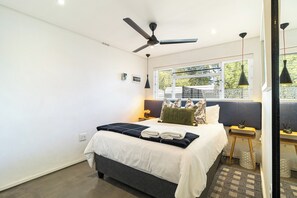 Ein modernes Hotelzimmer mit Bett, Deckenventilator, Nachttischen und einem Fenster mit Blick.