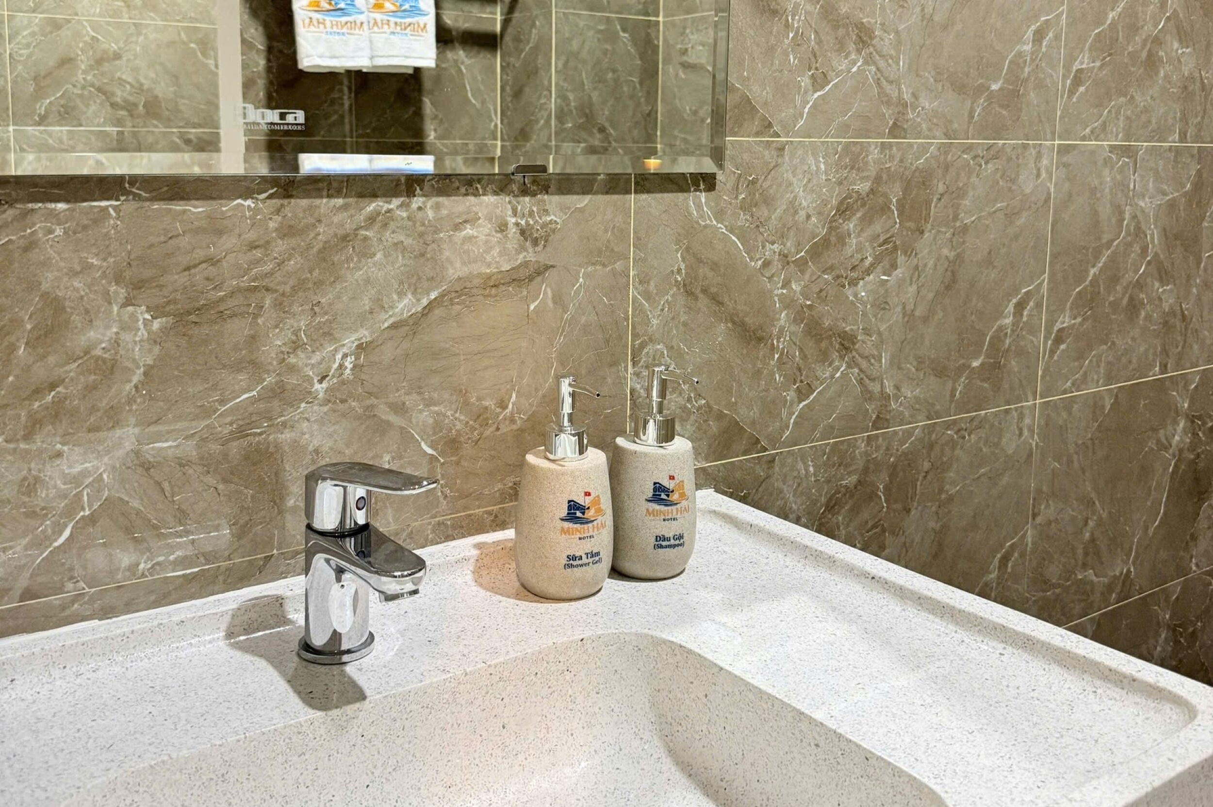 Un bagno con una parete in marmo, un lavandino, uno specchio e due flaconi di shampoo.