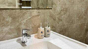 Un bagno con una parete in marmo, un lavandino, uno specchio e due flaconi di shampoo.