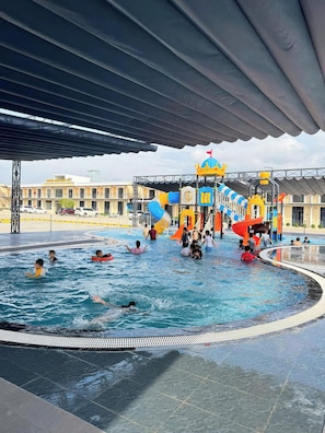 A swimming pool with a water slide and play structures, surrounded by a covered area.