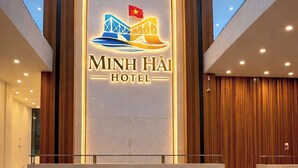 Un moderno vestíbulo de hotel con una recepción, un gran letrero iluminado que muestra el nombre del hotel y un techo alto con iluminación empotrada.