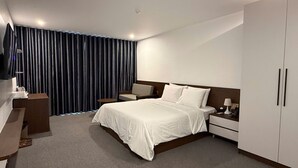 Una habitación de hotel moderna con una cama grande, un escritorio, una silla, un televisor y un armario.