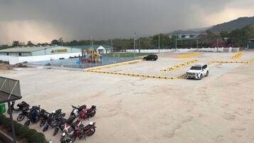 An outdoor parking area with motorcycles, a white SUV, and a building with a green roof.