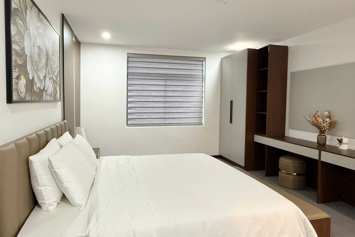 A bedroom with a bed, a window with blinds, a wardrobe, and a painting on the wall.
