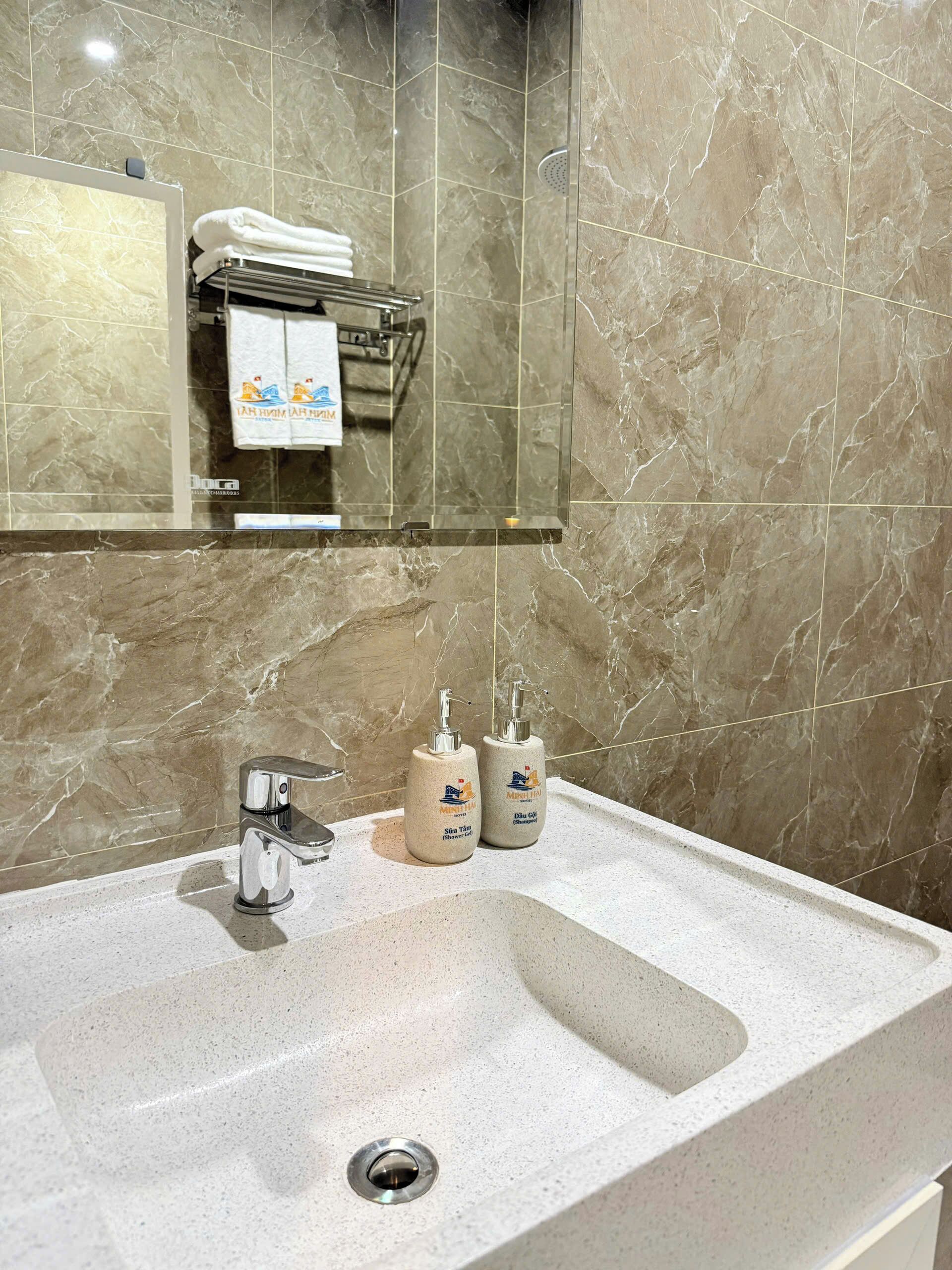 A bathroom with a marble sink, a mirror, a towel rack with towels, and two bottles of shower gel.