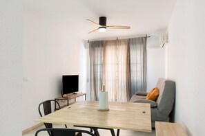 A modern living room with a dining table, a sofa, a TV, and a ceiling fan. - Apartment 'Las Flores 1' with Wi-Fi and Air Conditioning (Murcia)