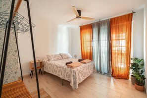 A bedroom with a bed, a standing fan, a side table, a lamp, and a potted plant. - Apartment 'Las Flores 1' with Wi-Fi and Air Conditioning (Murcia)