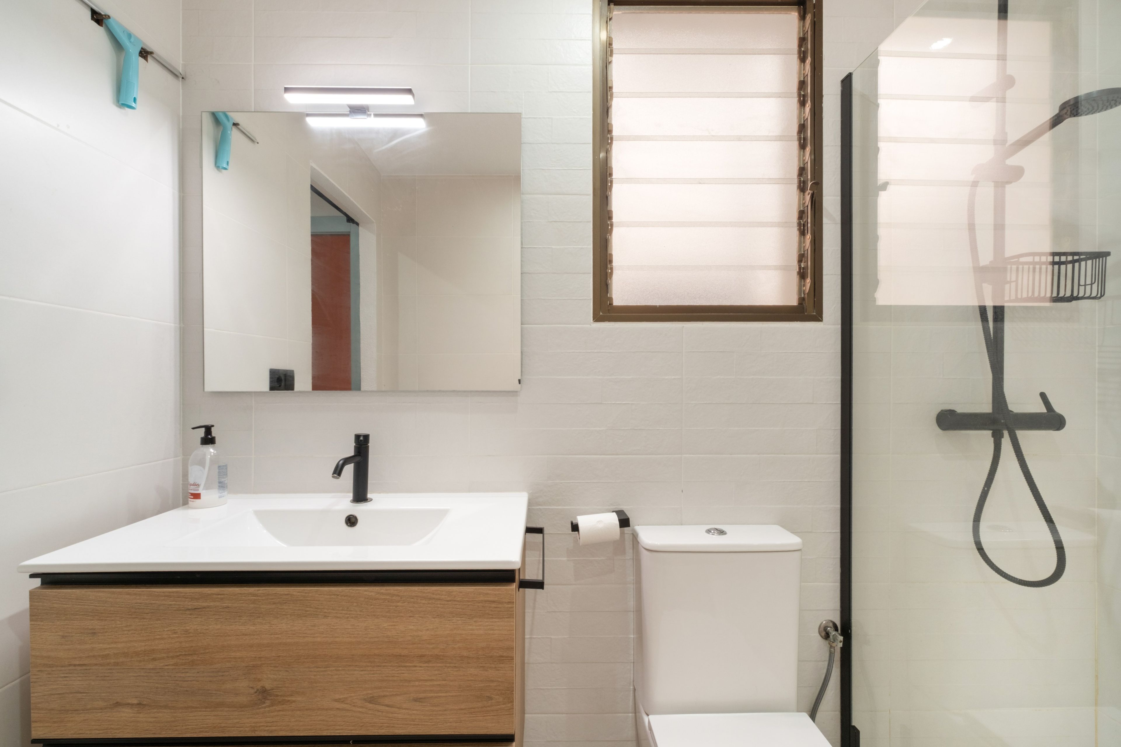 Un baño con lavamanos blanco, un espejo, un inodoro y una cabina de ducha con paredes de vidrio.