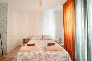 Een slaapkamer met een bed, kussens, een nachtkastje, een lamp en een raam met gordijnen.