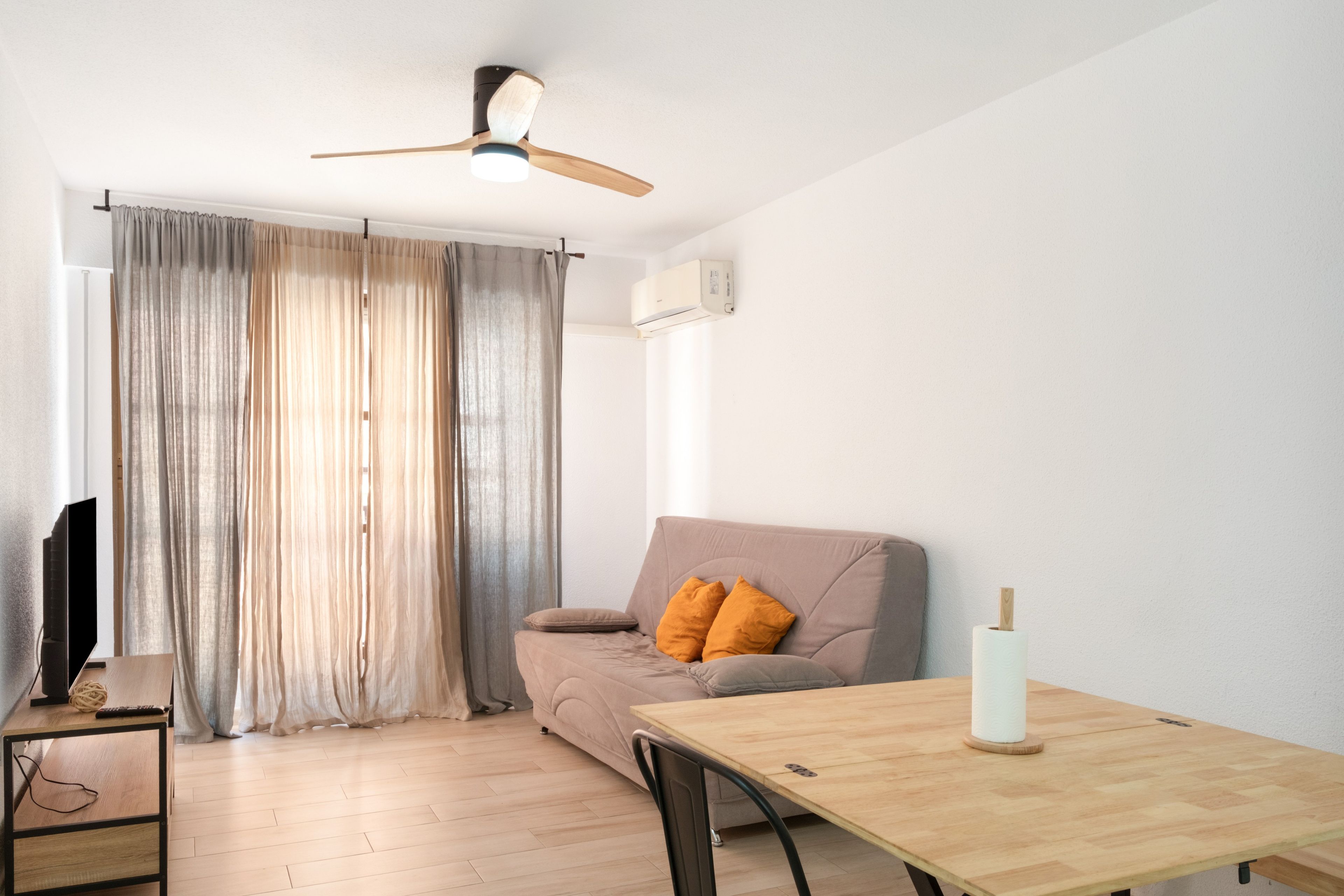 A living room with a sofa, a wooden table, a ceiling fan, and a TV.