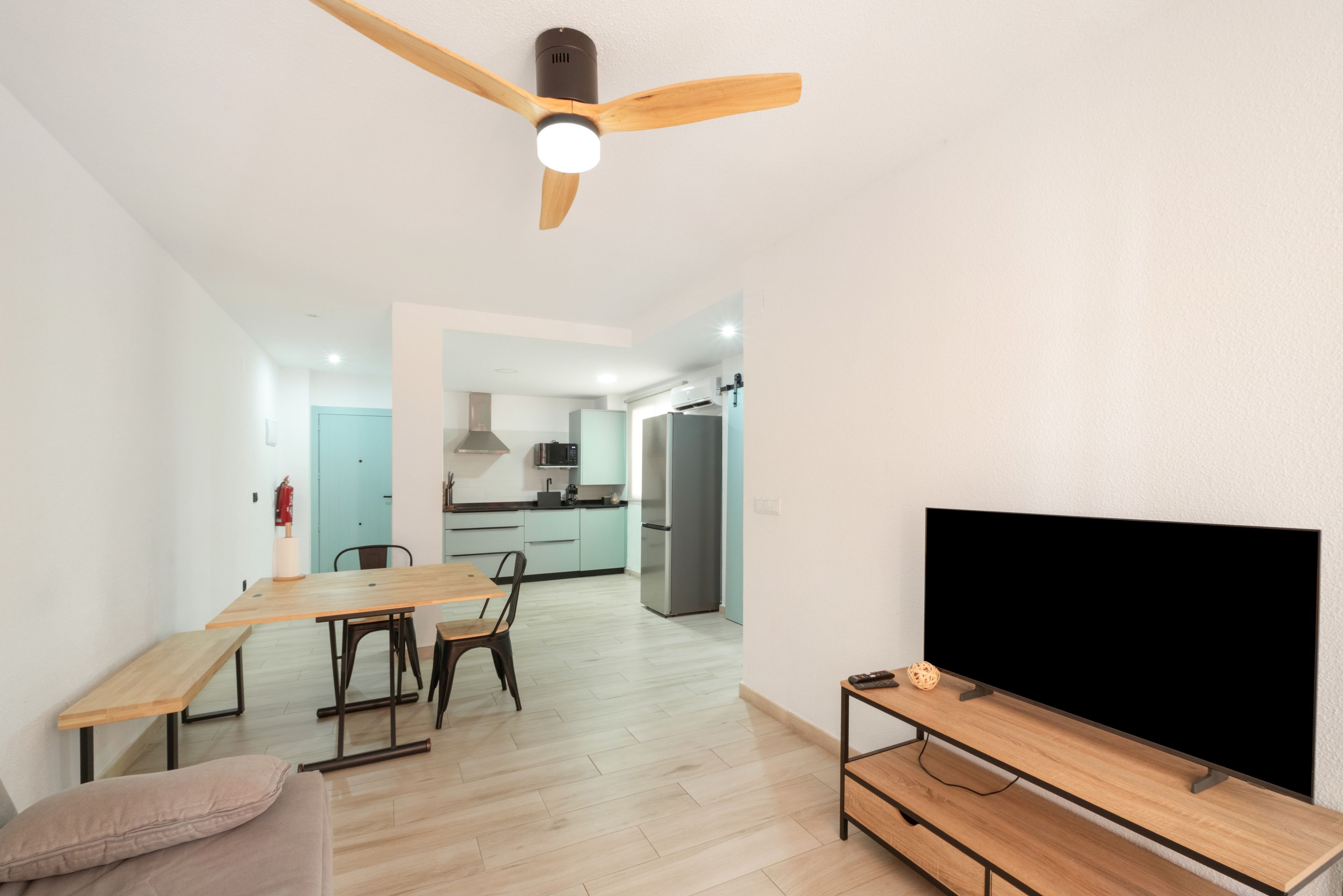Una sala de estar moderna con comedor, una cocina al fondo y un televisor de pantalla plana sobre un soporte de madera.