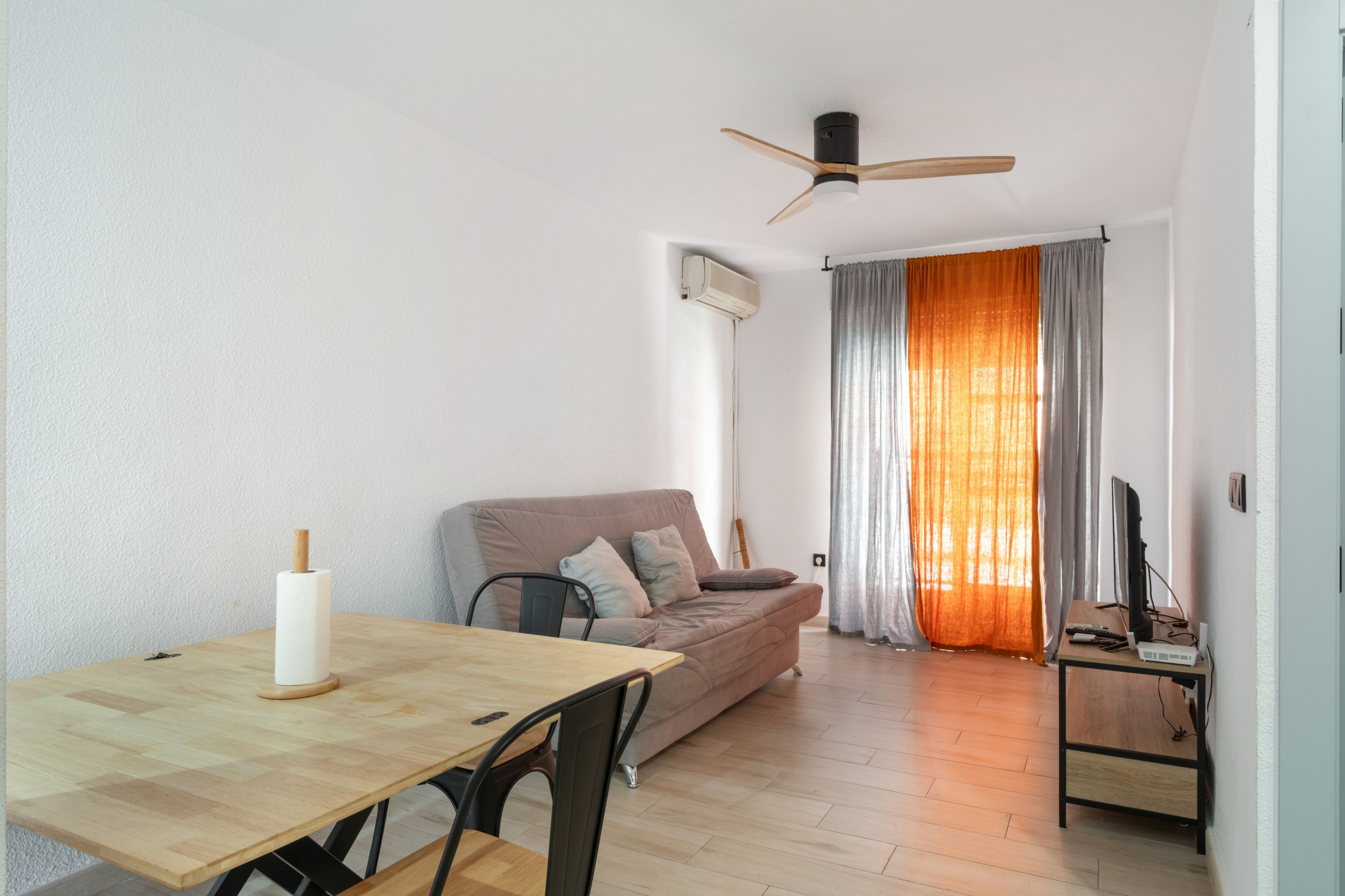 Un salon comprenant un canapé, une table à manger, un ventilateur de plafond et un téléviseur.