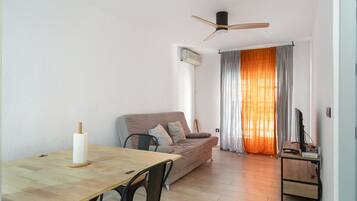 Un salon comprenant un canapé, une table à manger, un ventilateur de plafond et un téléviseur.