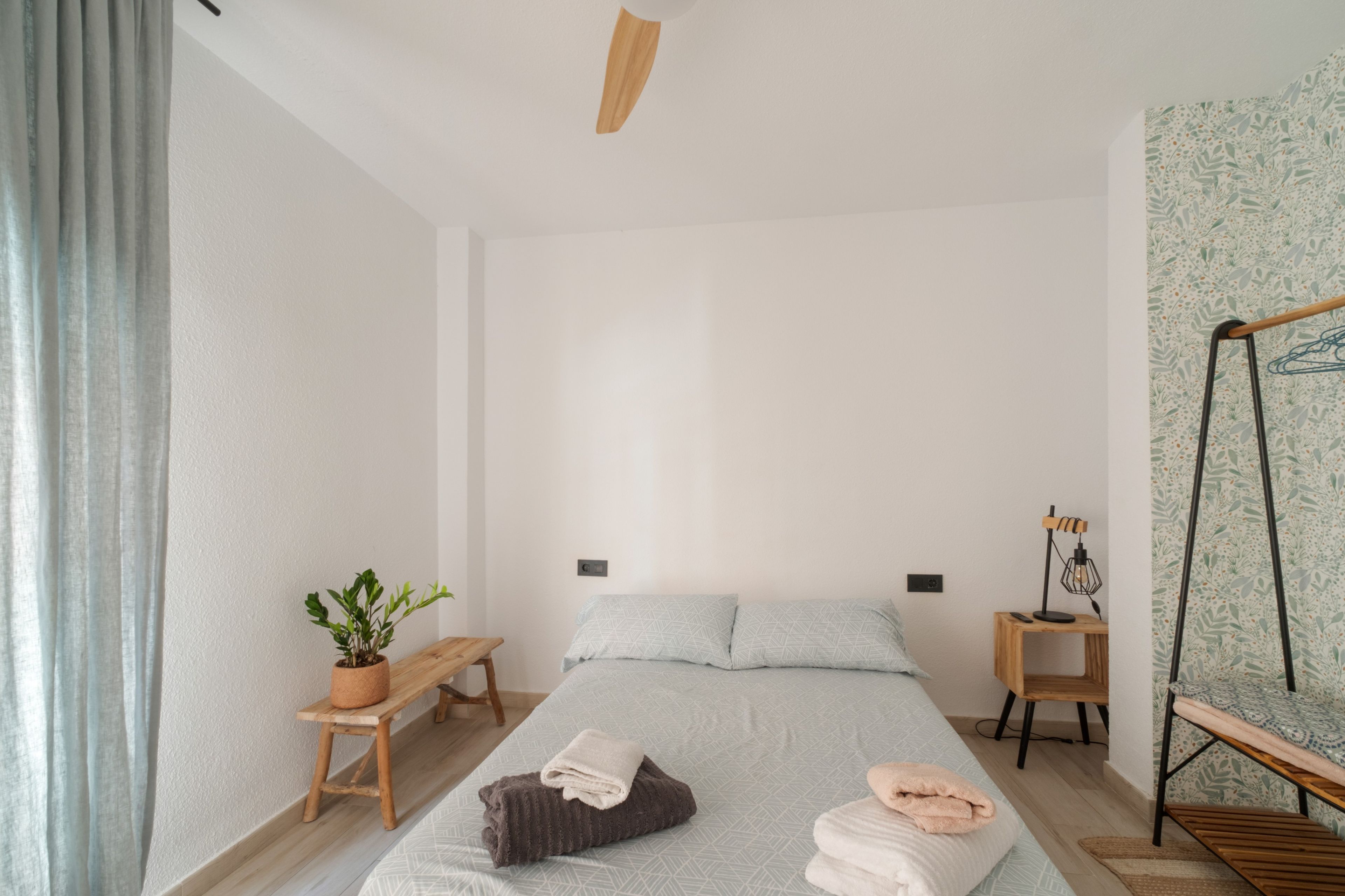 Une chambre à coucher au style minimaliste, avec un lit simple, des tables de chevet, une lampe suspendue et une plante en pot.