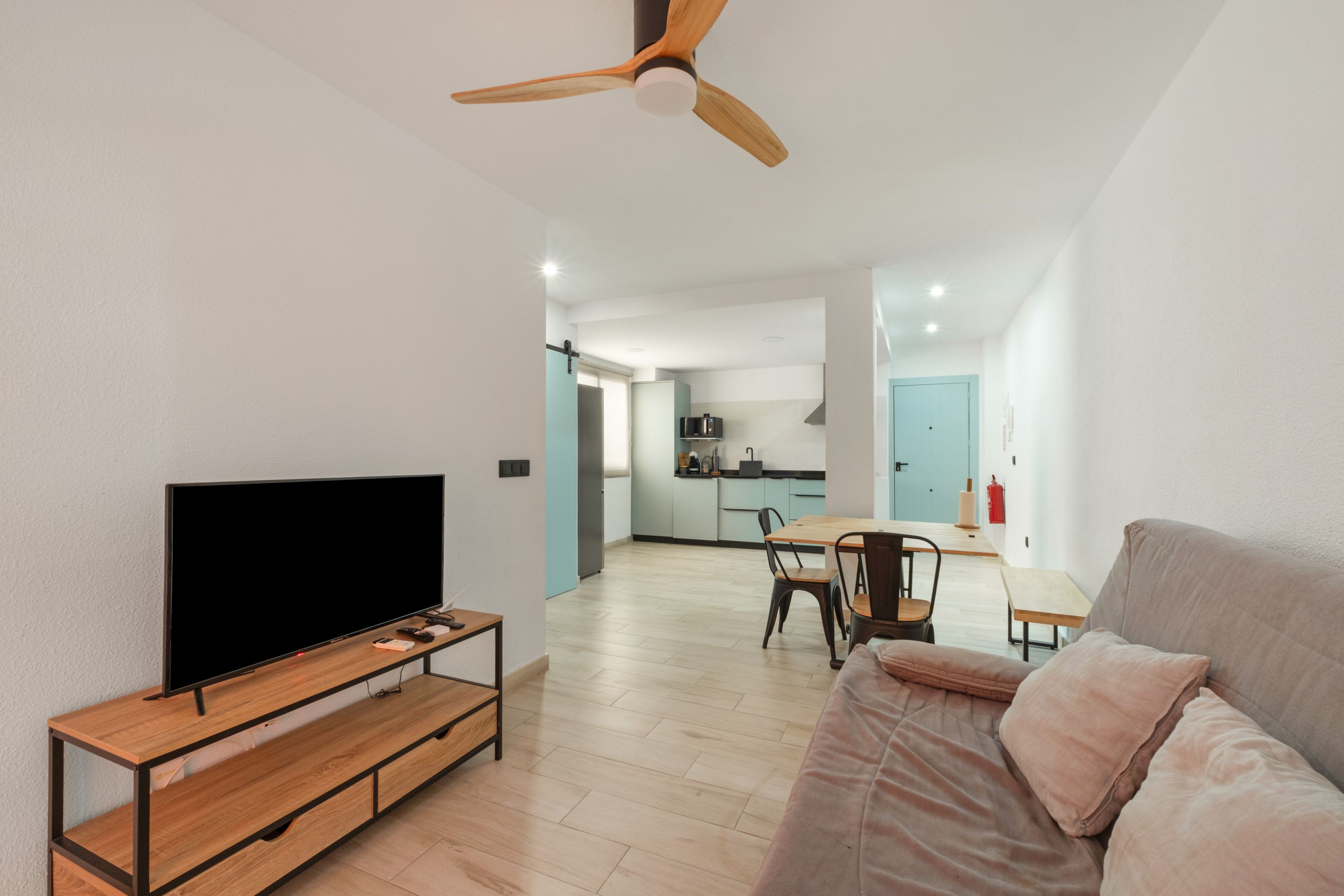 A modern living room with a flat-screen TV, wooden entertainment unit, and a ceiling fan.