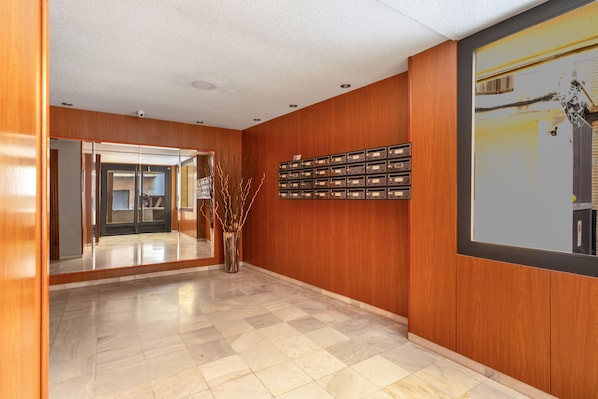 A lobby with a checkered floor, wooden walls, a mirror, a vase with branches, and a wall-mounted mailbox.