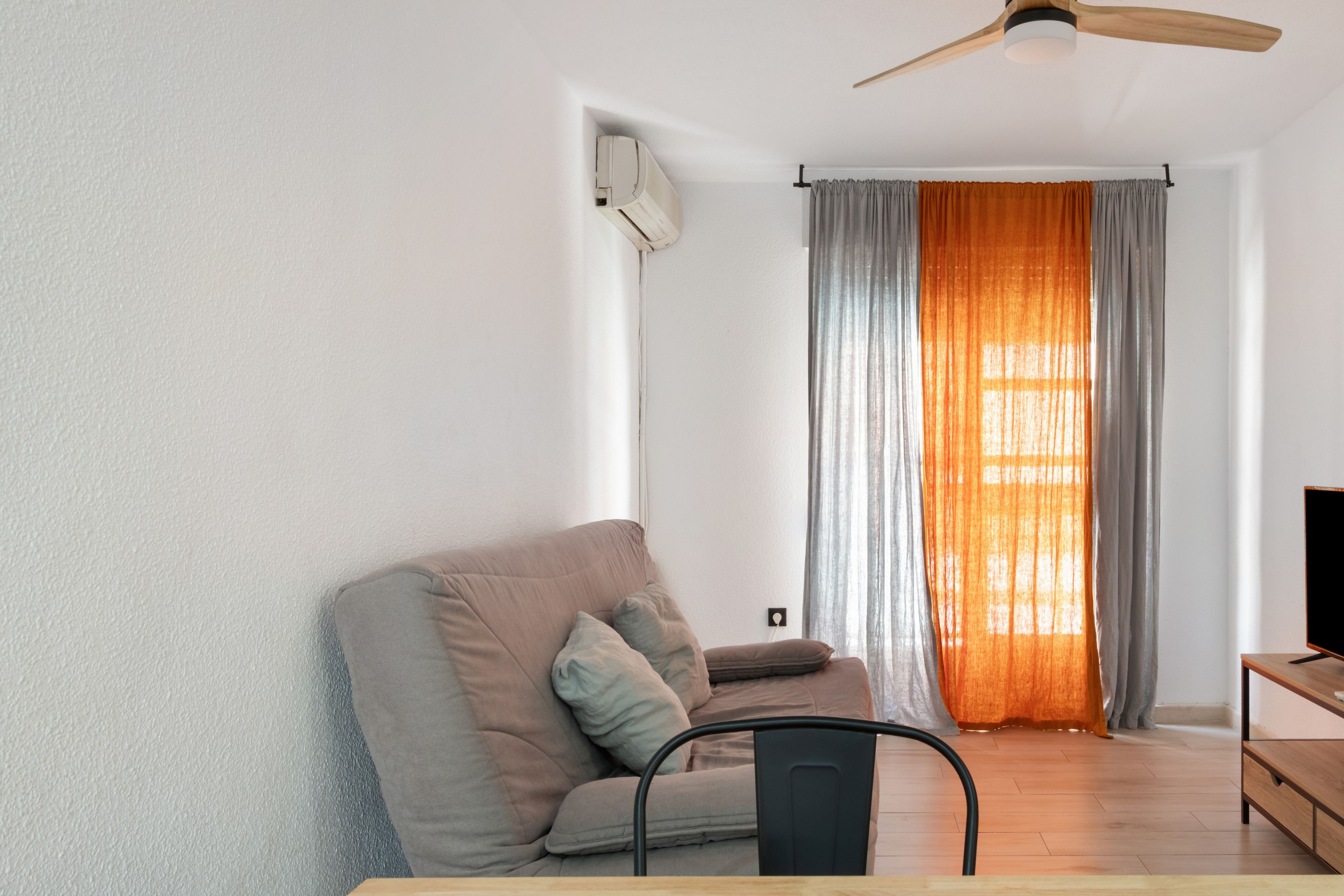 Una sala de estar con un sofá, un mueble para televisión y un ventilador de techo.