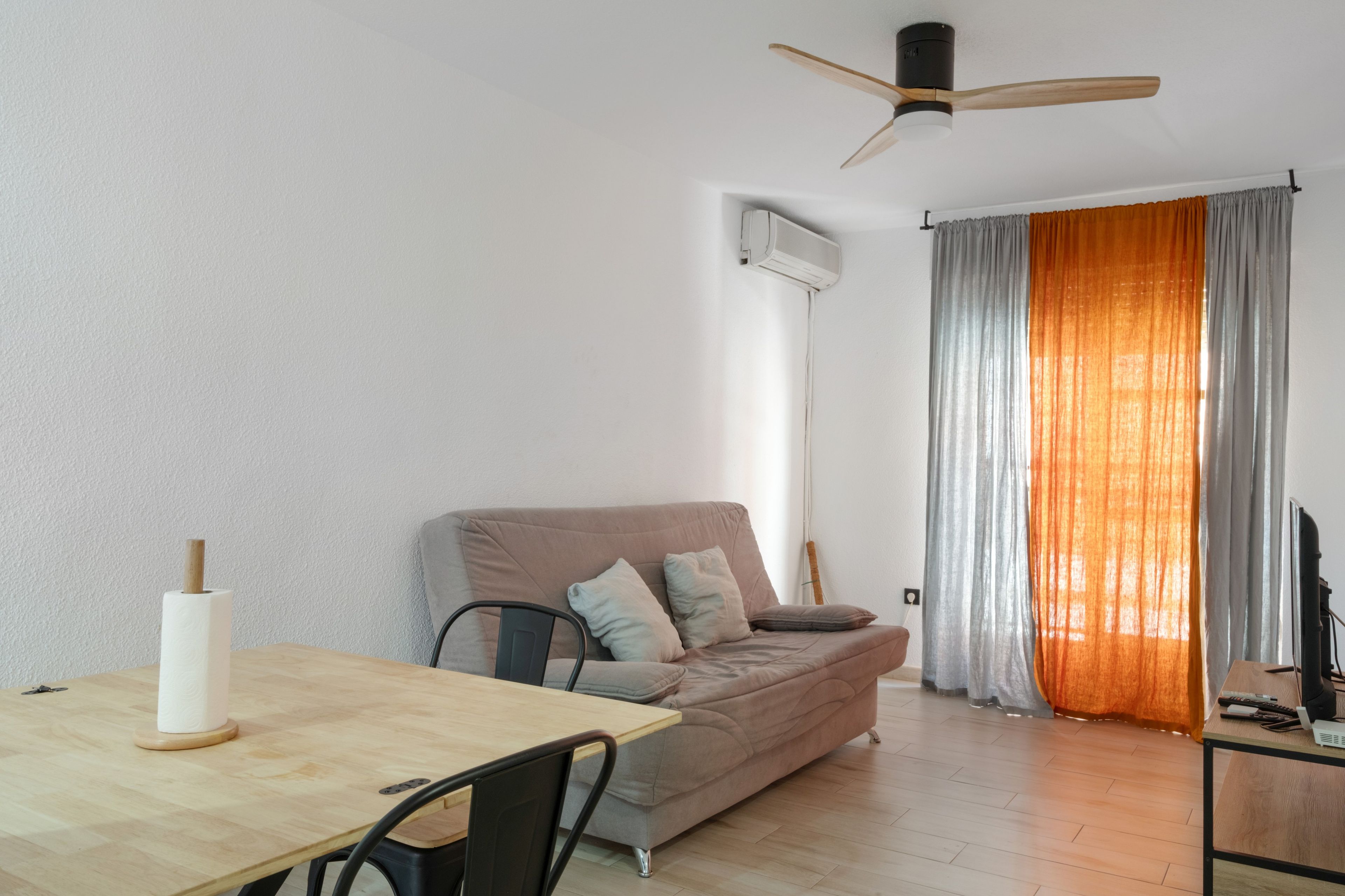 Ein zeitgemäßer Wohnraum mit einer Couch, einem Esstisch und einem Deckenventilator.