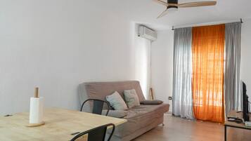Un espai de vida modern amb un sofà, una taula de dinar i un ventilador de sostre.